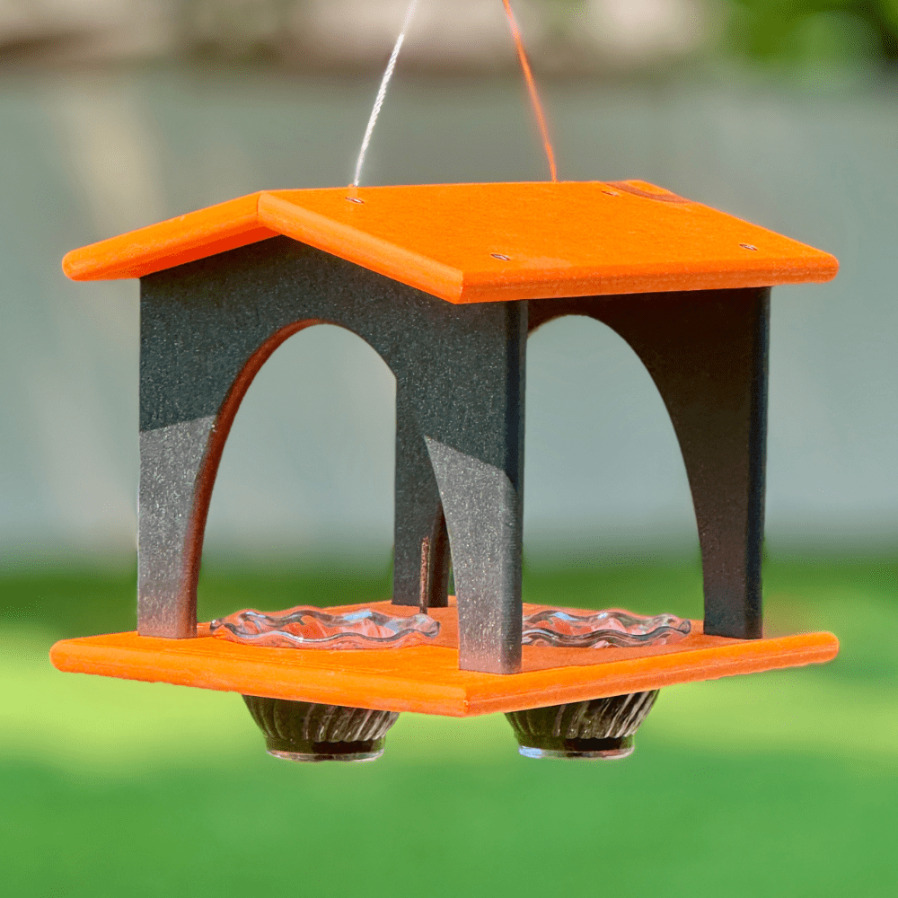 Bird feeder with orange and black design hanging against a blurred natural background